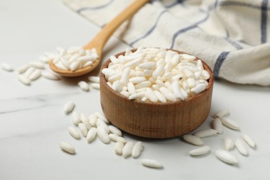 Photo of Puffed rice in bowl and spoon on white marble table, closeup