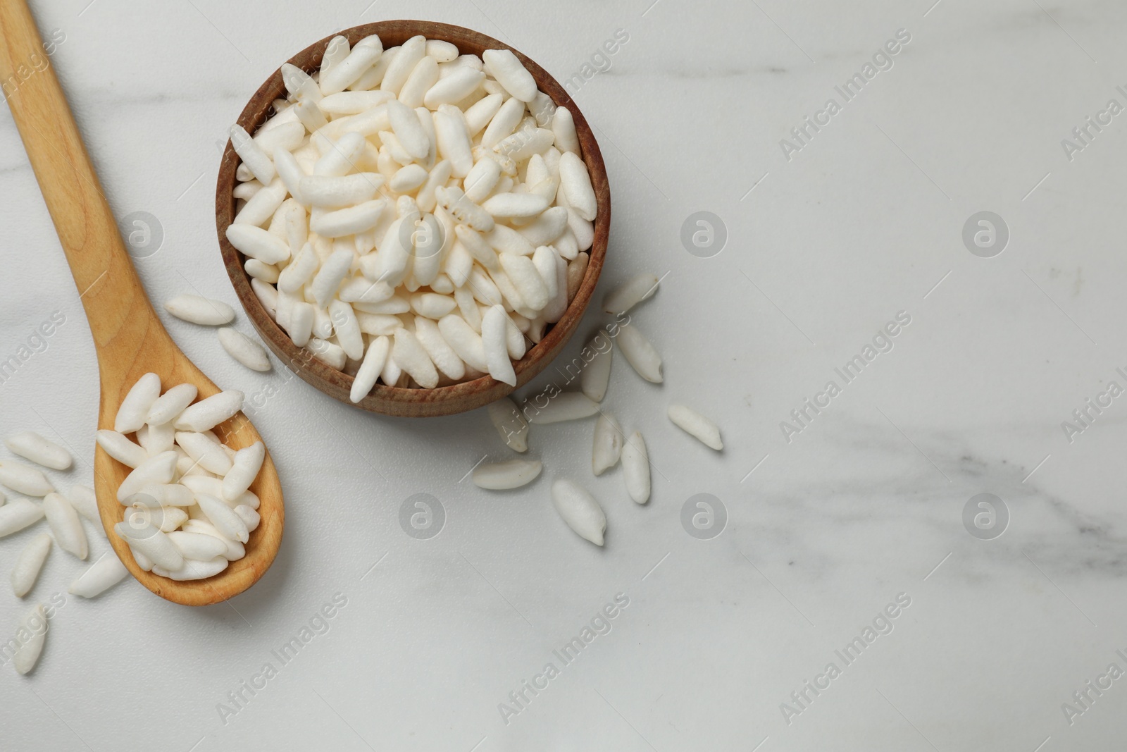 Photo of Puffed rice in bowl and spoon on white marble table, flat lay. Space for text