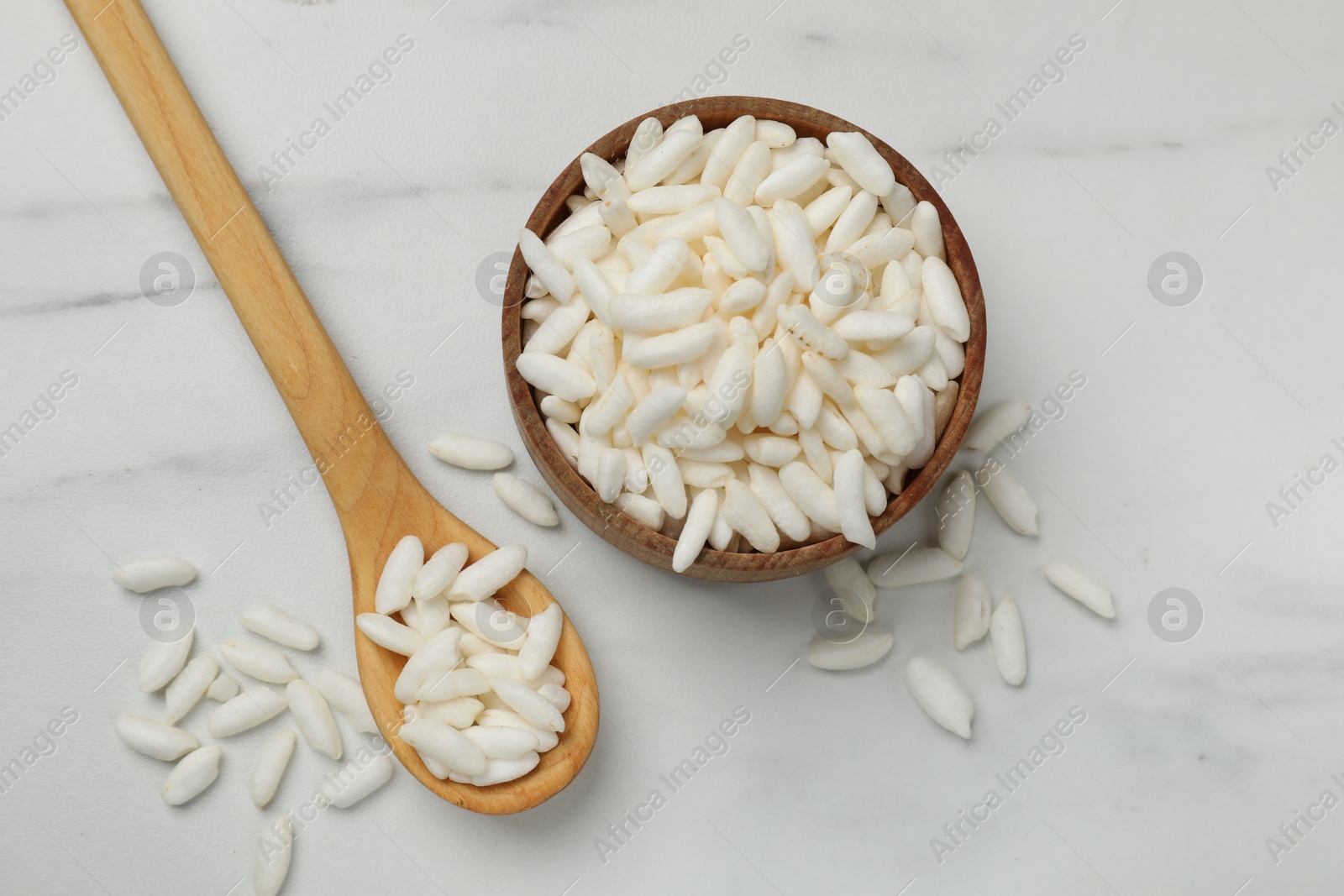 Photo of Puffed rice in bowl and spoon on white marble table, flat lay