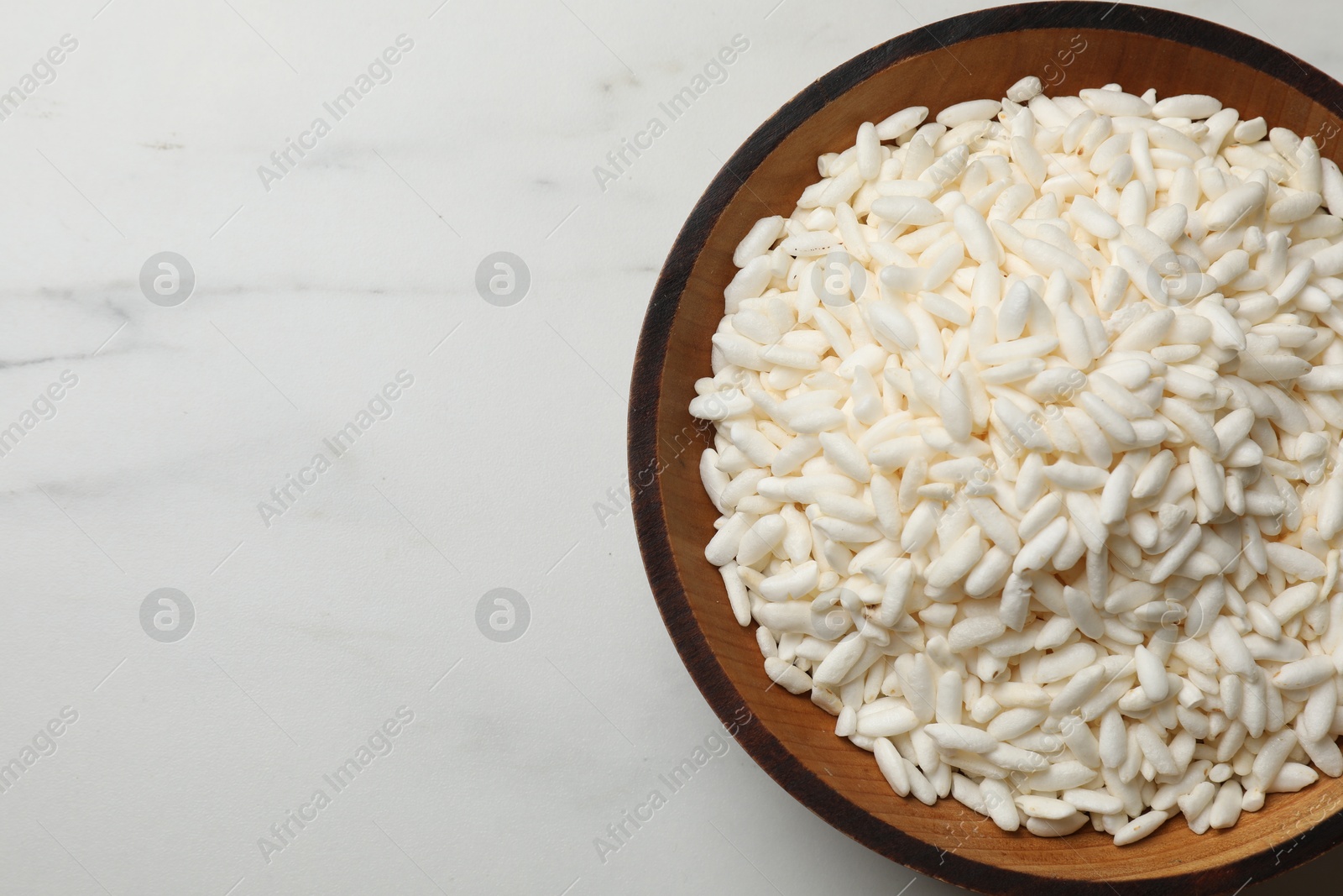 Photo of Puffed rice in bowl on white marble table, top view. Space for text