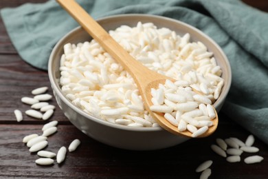 Photo of Puffed rice in bowl and spoon on wooden table, closeup