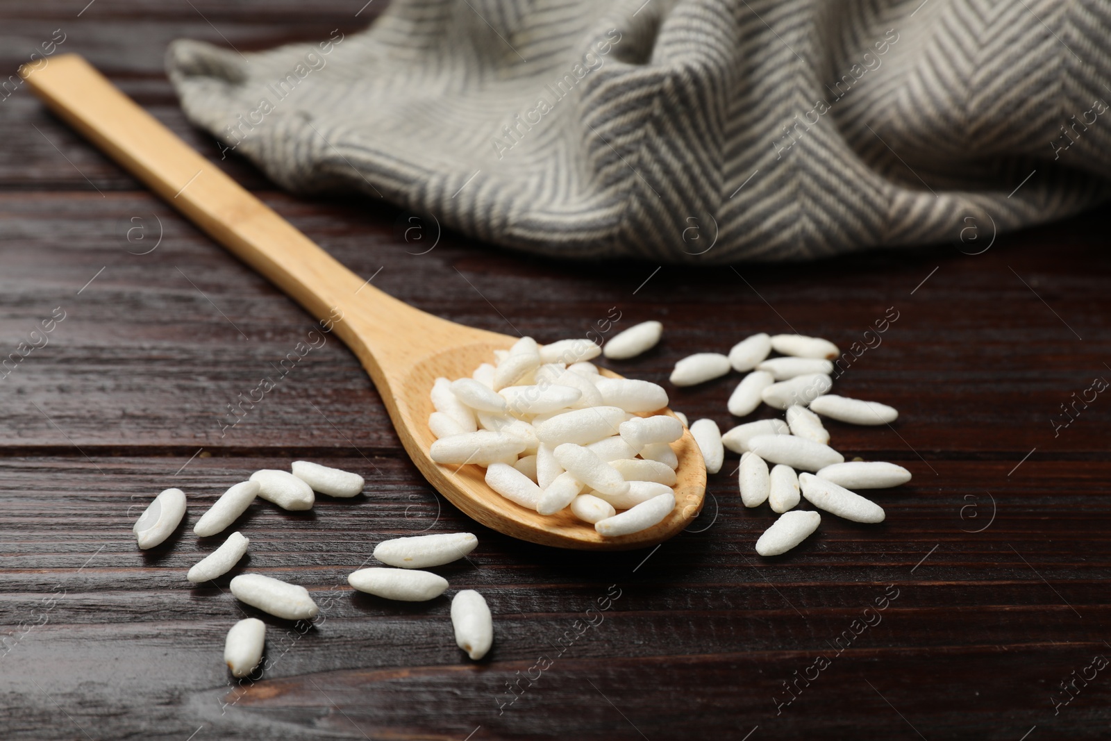 Photo of Puffed rice in spoon on wooden table, closeup