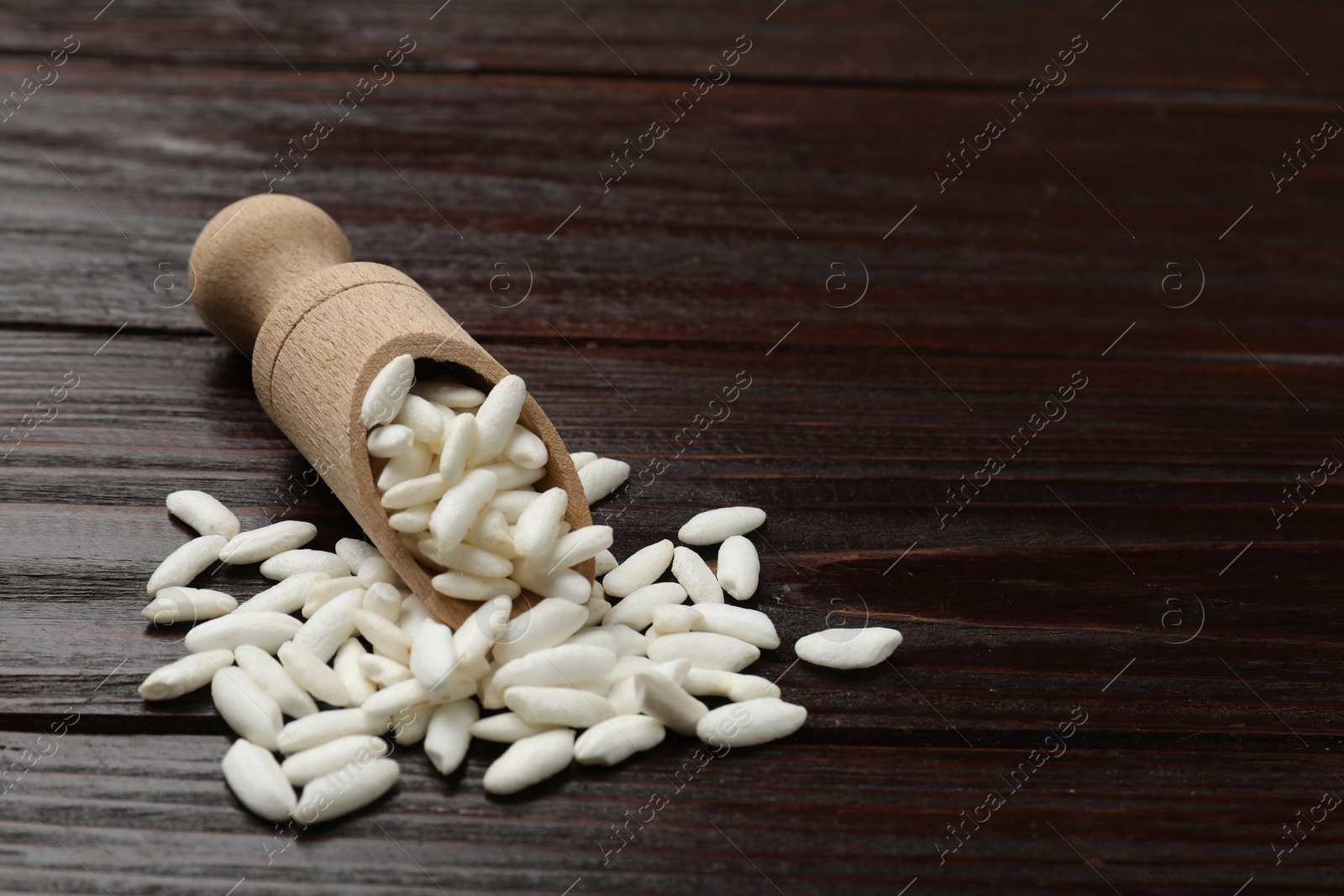 Photo of Puffed rice in scoop on wooden table, closeup. Space for text