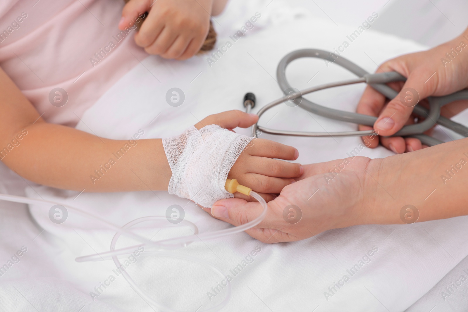 Photo of Doctor examining little girl and setting IV drip on bed at hospital, closeup