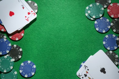 Frame of poker chips and playing cards on green table, flat lay. Space for text