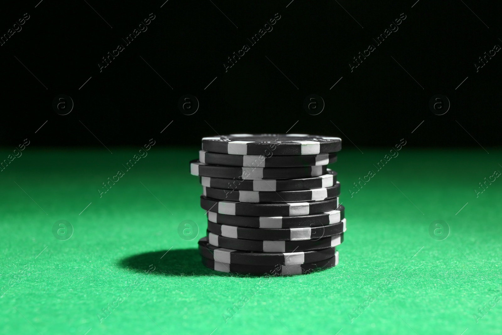 Photo of Stack of poker chips on green table against dark background, closeup