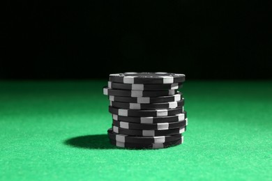 Stack of poker chips on green table against dark background, closeup