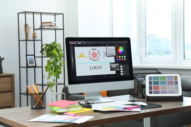 Photo of Designer's workplace with computer, tablet, color palettes and stationery on wooden table indoors