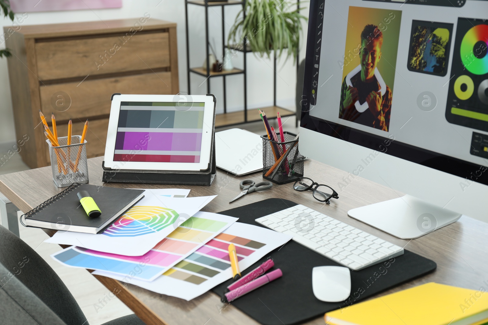 Photo of Designer's workplace with computer, tablet, color palettes and stationery on wooden table indoors