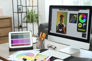 Photo of Designer's workplace with computer, tablet, color palettes and stationery on wooden table indoors