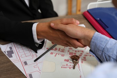 Photo of Real estate agent shaking hands with client at wooden table, closeup