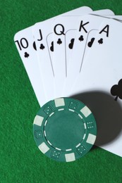 Playing cards and poker chips on green table, top view