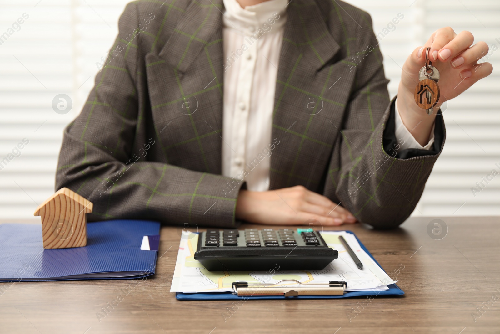 Photo of Real estate agent with house model, key and stationery at wooden table, closeup