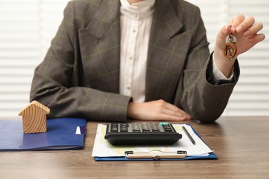 Real estate agent with house model, key and stationery at wooden table, closeup