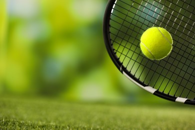 Photo of Tennis racket with ball on green artificial grass, closeup. Space for text