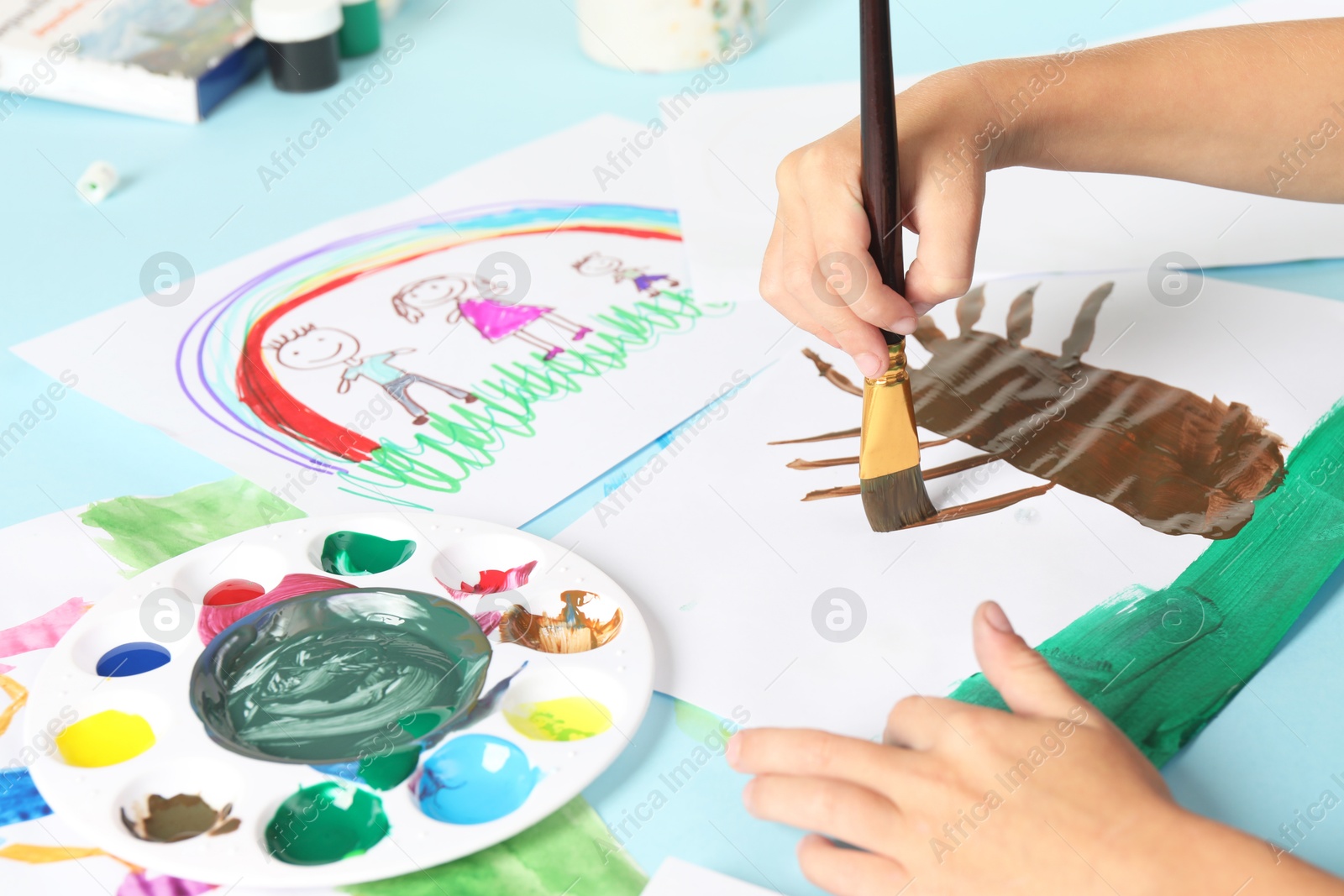 Photo of Boy drawing picture with paint at light blue table, closeup