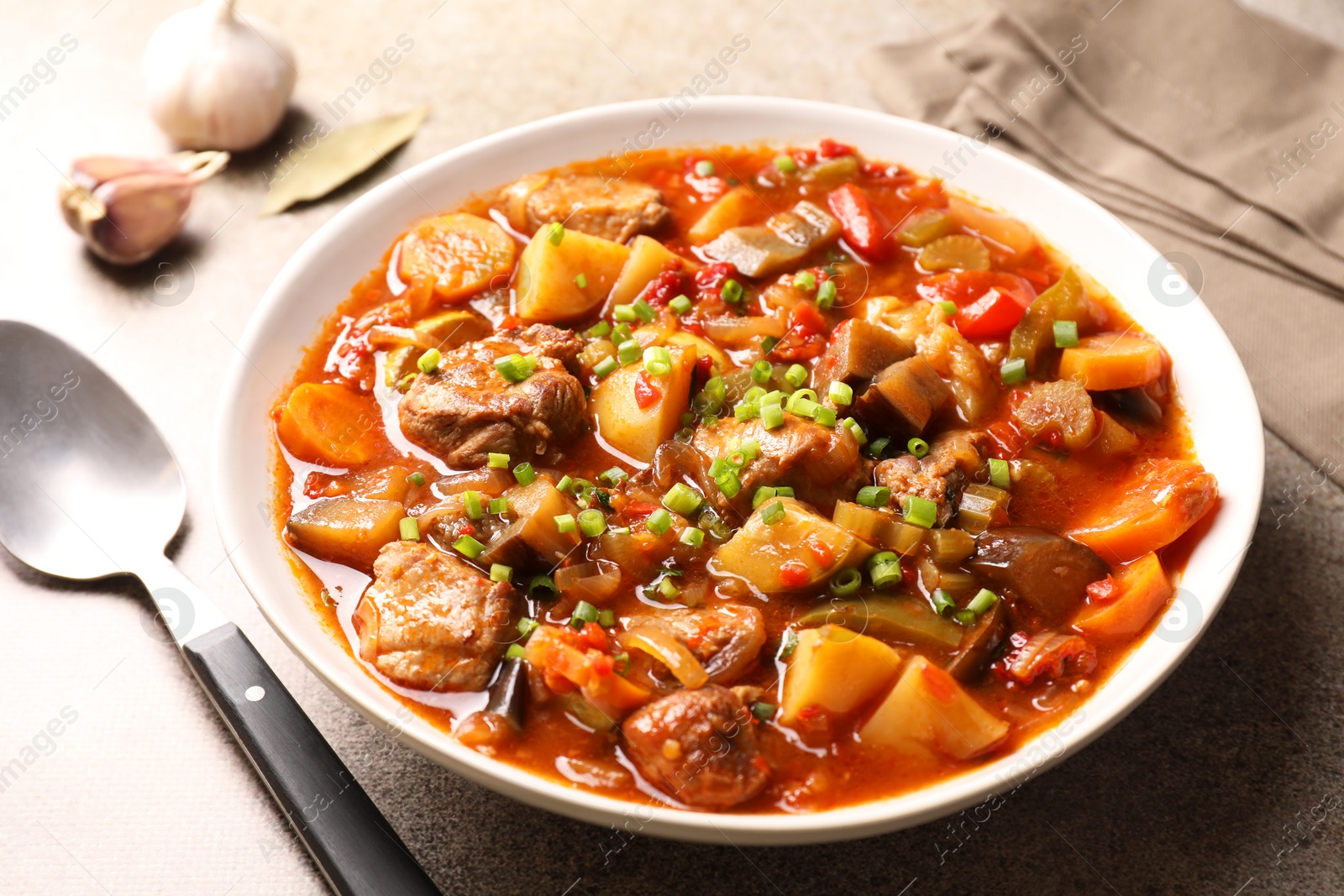 Photo of Delicious stew with vegetables in bowl and spoon on light grey table, closeup