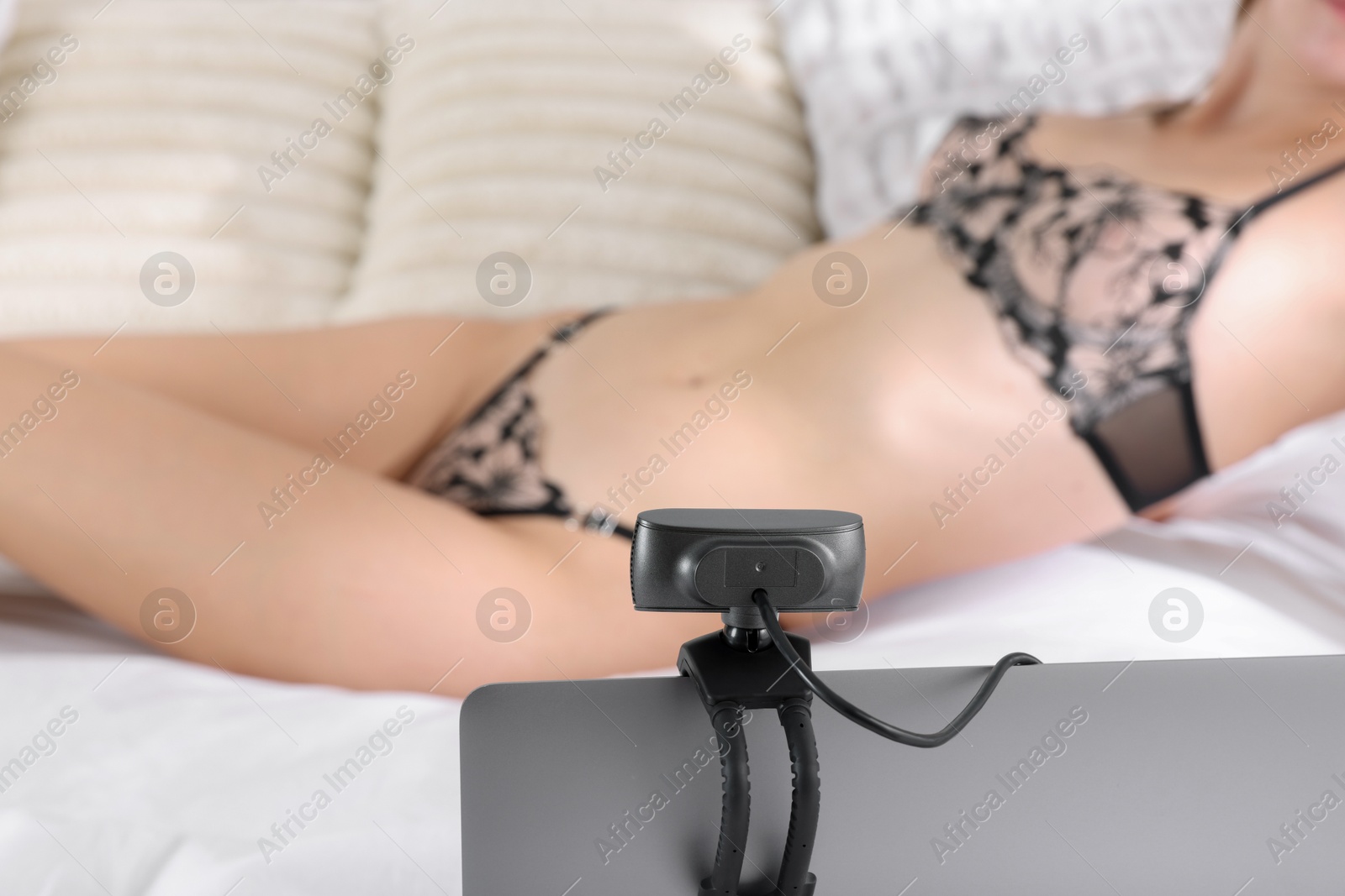 Photo of Prostitution. Webcam model in underwear streaming with laptop on bed indoors, selective focus