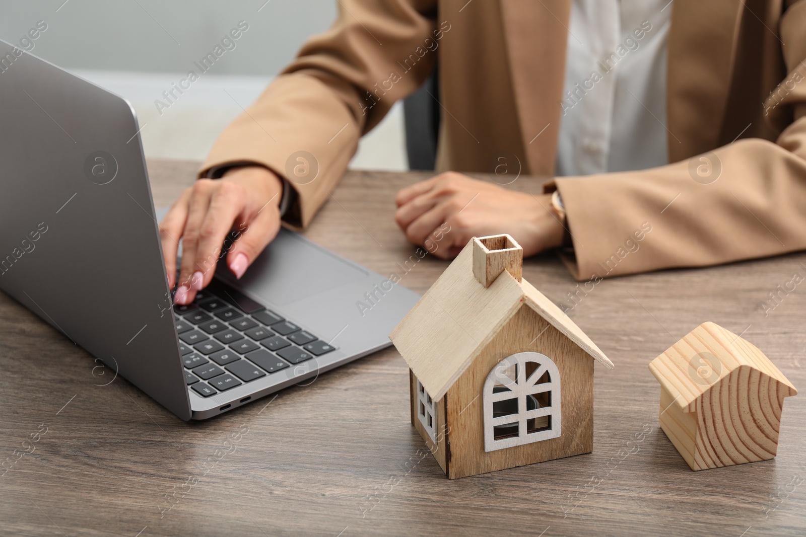 Photo of House hunting. Woman with laptop and house figures at wooden table, closeup