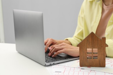 Photo of House hunting. Woman with laptop, papers and house figure at white table, closeup