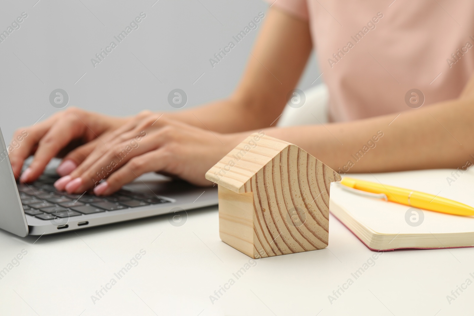 Photo of House hunting. Woman with laptop, notebook and house figure at white table, closeup