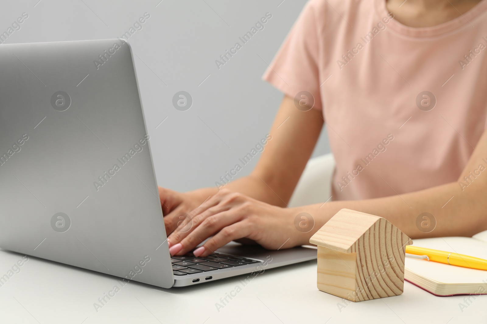 Photo of House hunting. Woman with laptop, notebook and house figure at white table, closeup