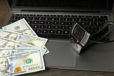 Photo of Sex work. Laptop with web camera and money on wooden surface, closeup