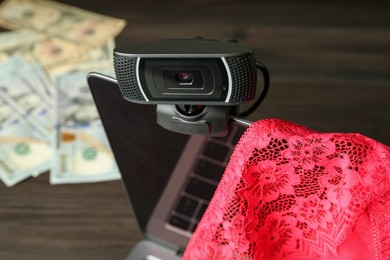 Photo of Sex work. Laptop with web camera and panties on wooden surface, closeup