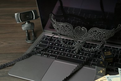 Photo of Sex work. Laptop with mask on wooden surface, closeup