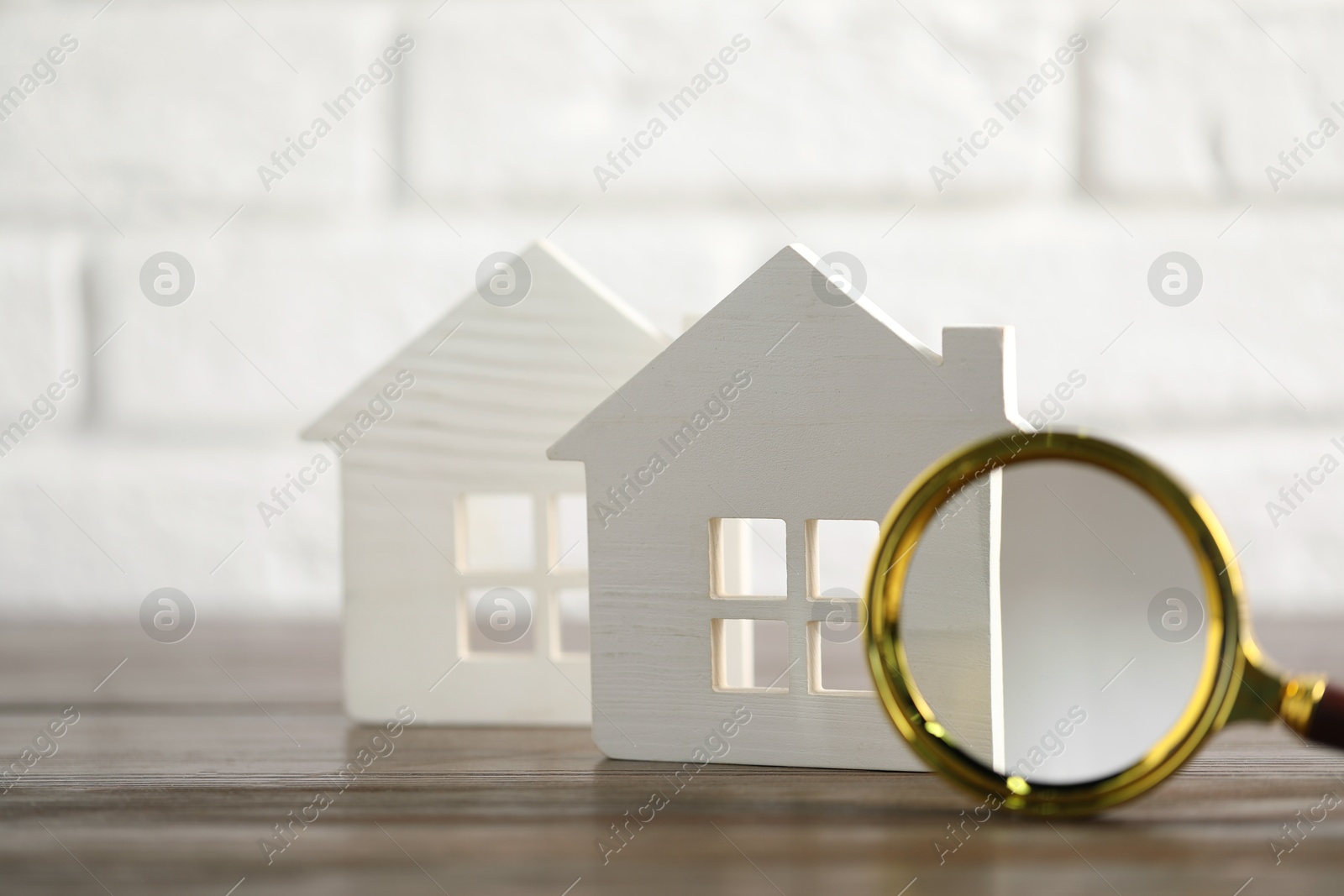 Photo of House hunting. Magnifying glass and house figures on wooden table