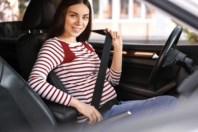 Smiling pregnant woman fastening safety belt in car