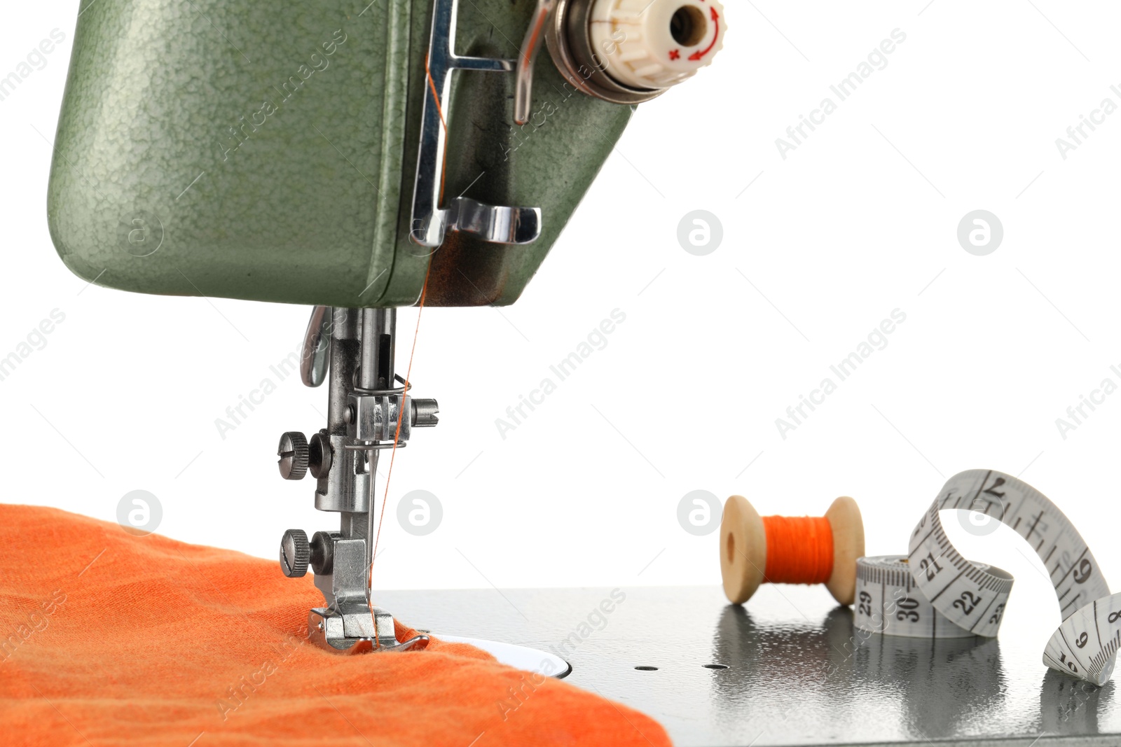 Photo of Sewing machine with orange fabric, measuring tape and spool of thread isolated on white