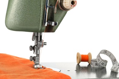 Photo of Sewing machine with orange fabric, measuring tape and spool of thread isolated on white