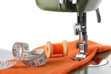 Photo of Sewing machine with orange fabric, measuring tape and spool of thread isolated on white