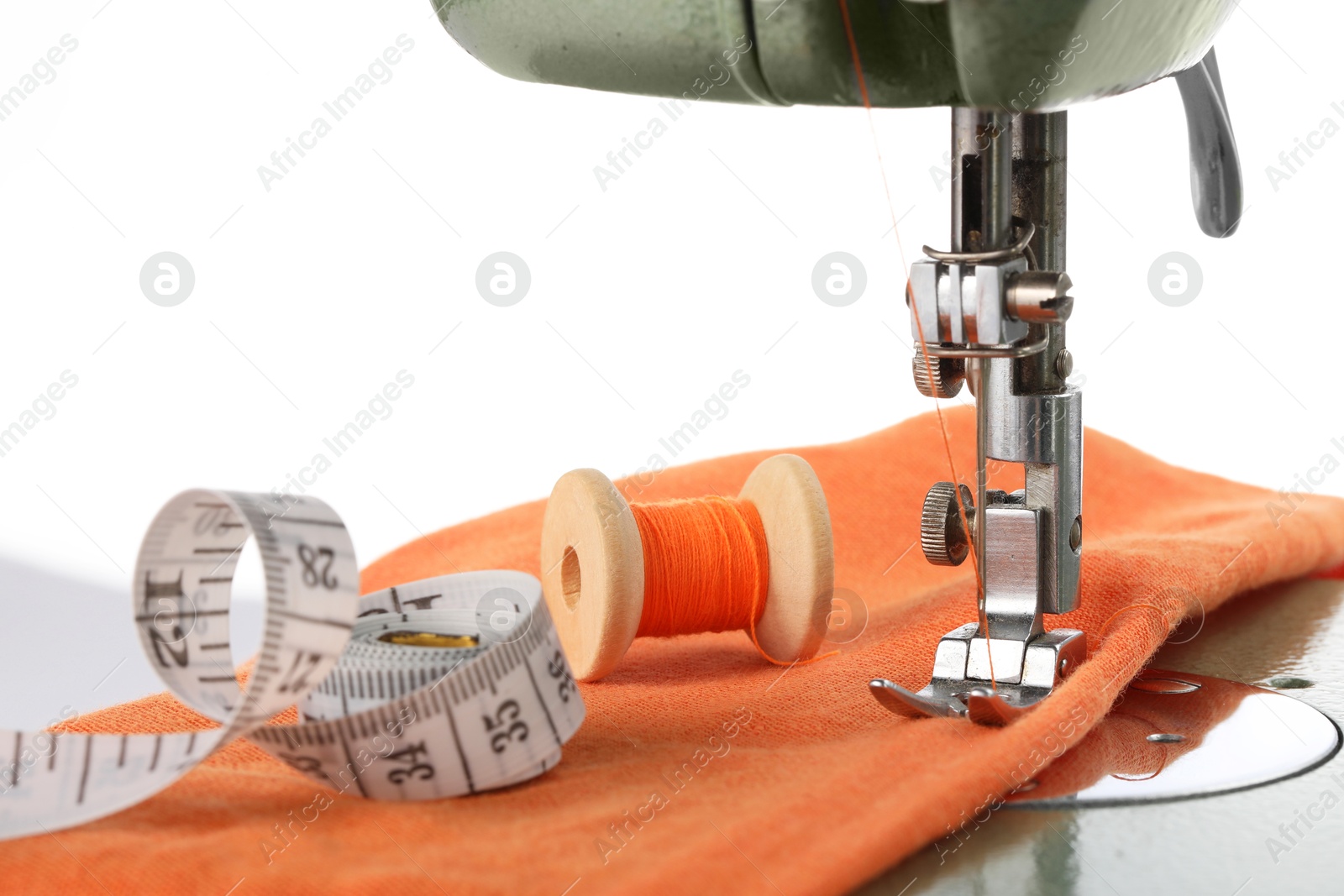 Photo of Sewing machine with orange fabric, measuring tape and spool of thread isolated on white