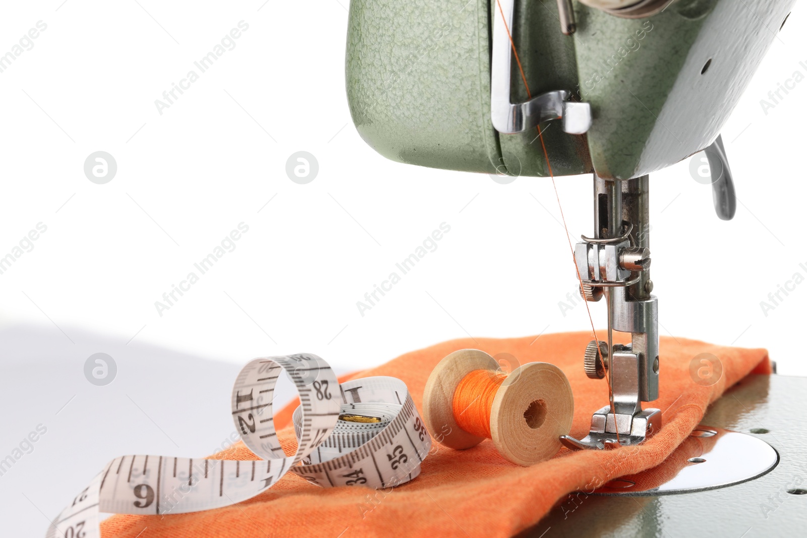 Photo of Sewing machine with orange fabric, measuring tape and spool of thread isolated on white