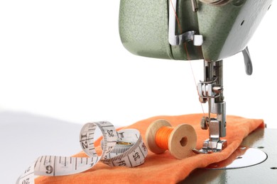 Photo of Sewing machine with orange fabric, measuring tape and spool of thread isolated on white