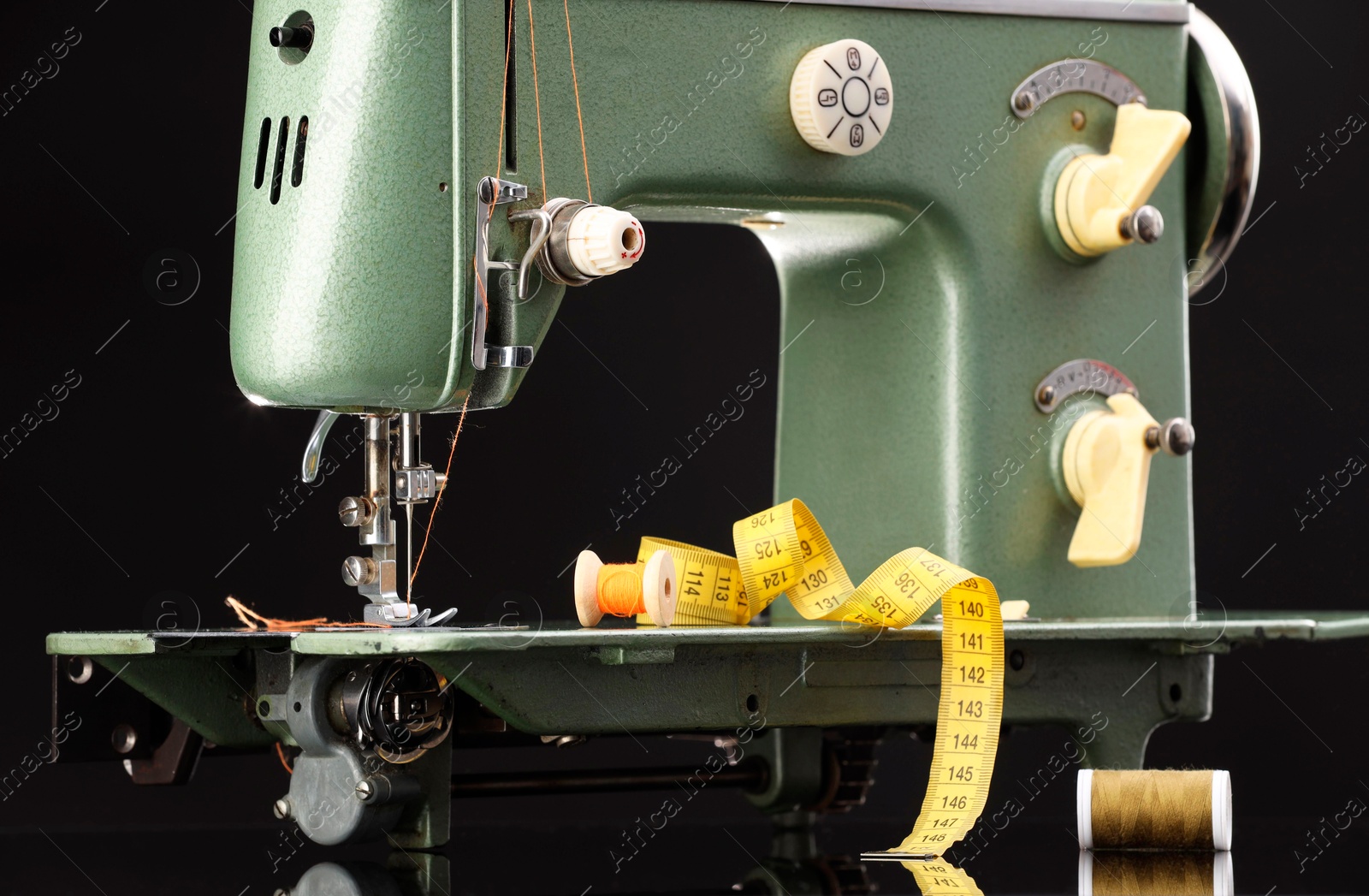 Photo of Professional sewing machine and measuring tape on black background, closeup