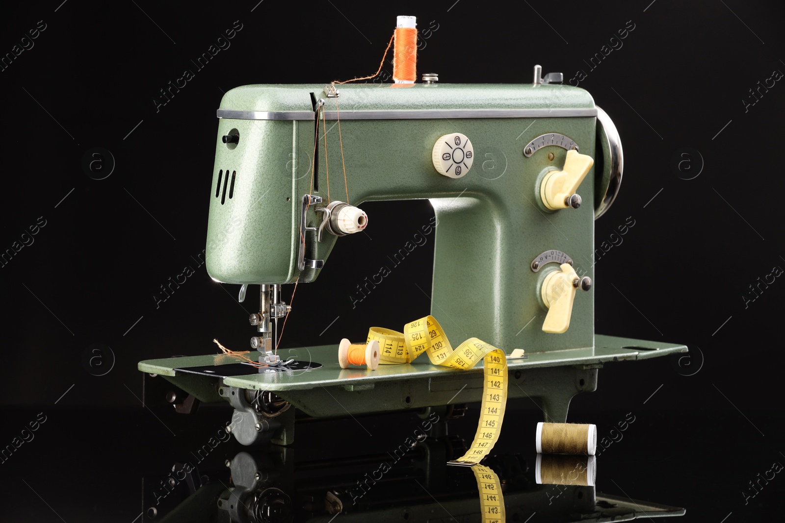 Photo of Professional sewing machine and measuring tape on black background