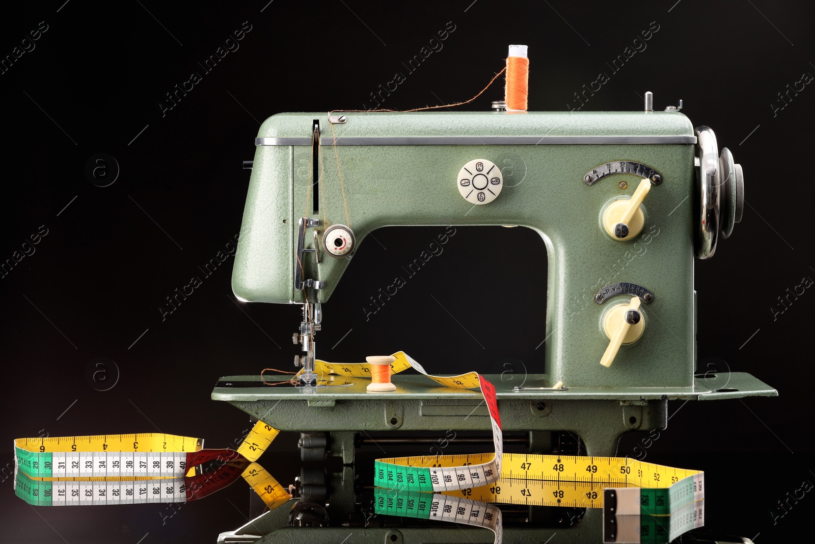 Photo of Professional sewing machine and measuring tape on black background