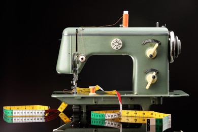 Photo of Professional sewing machine and measuring tape on black background