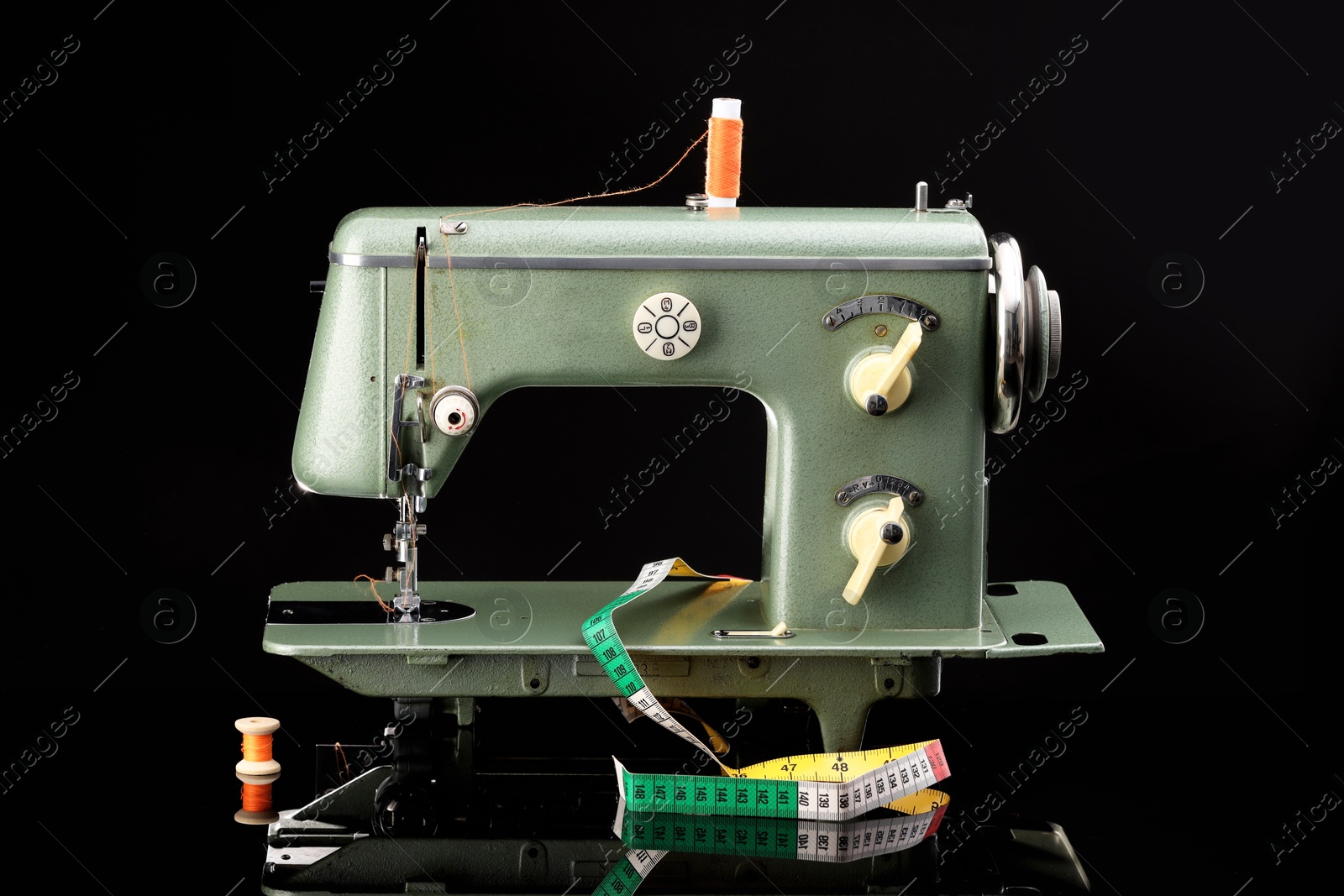 Photo of Professional sewing machine and measuring tape on black background