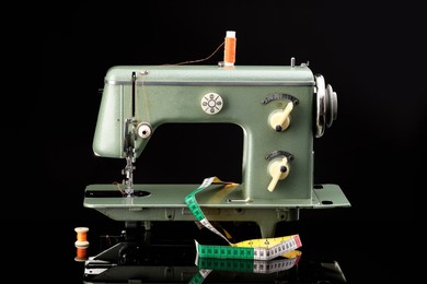 Photo of Professional sewing machine and measuring tape on black background