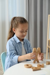 Photo of Little girl learning alphabet with wooden letters at white table indoors