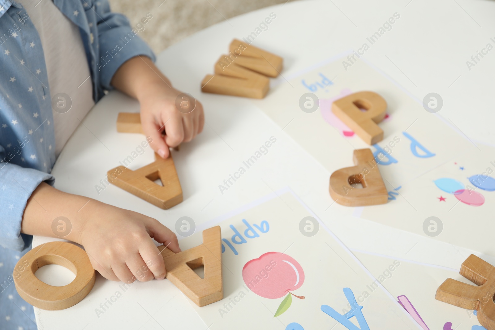 Photo of Little girl learning alphabet with wooden letters at white table indoors, closeup