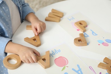 Photo of Little girl learning alphabet with wooden letters at white table indoors, closeup