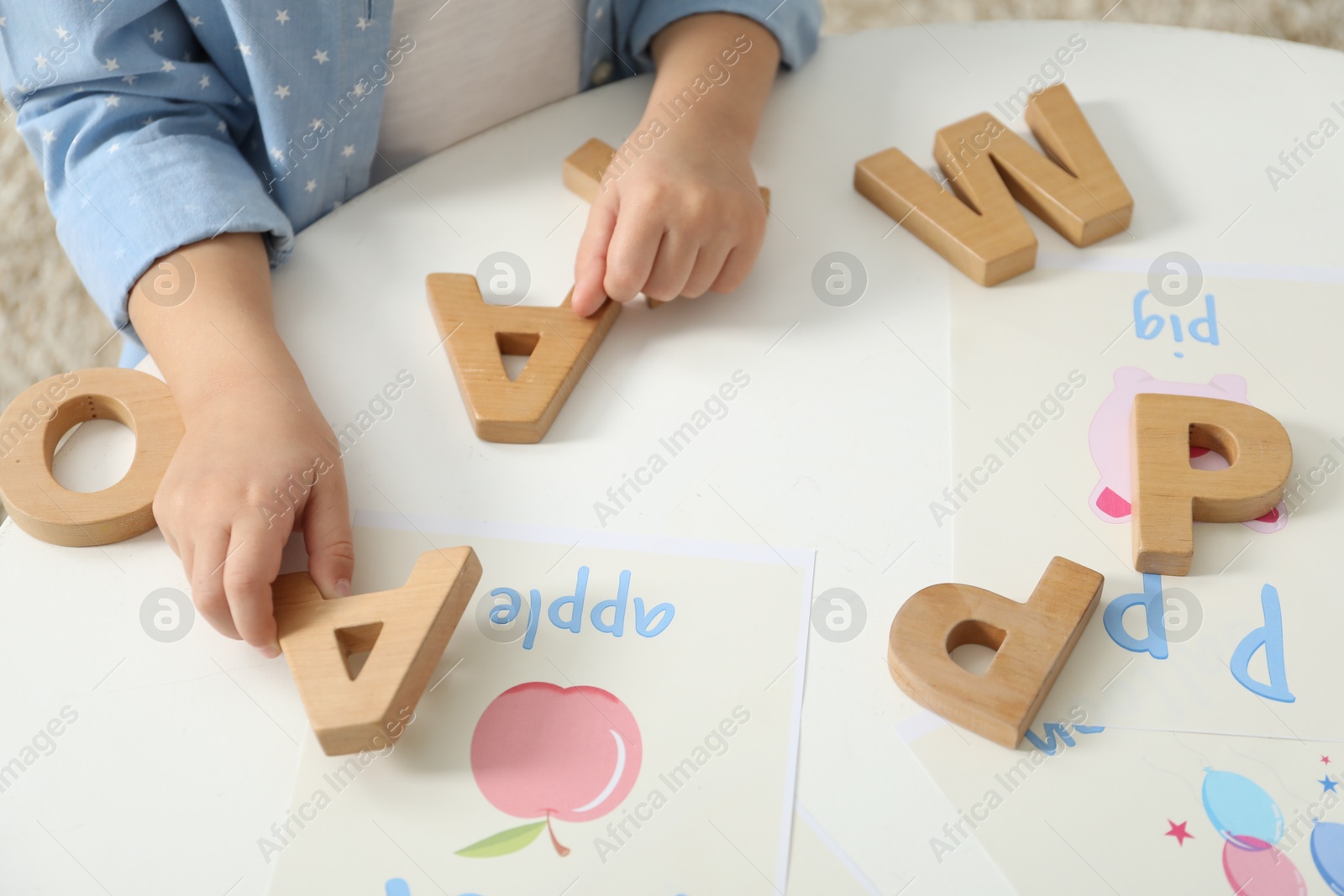 Photo of Little girl learning alphabet with wooden letters at white table indoors, closeup