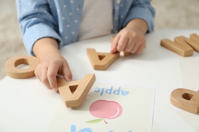 Photo of Little girl learning alphabet with wooden letters at white table indoors, closeup