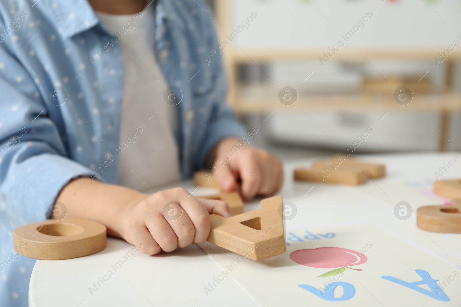 Photo of Little girl learning alphabet with wooden letters at white table indoors, closeup