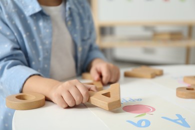 Photo of Little girl learning alphabet with wooden letters at white table indoors, closeup